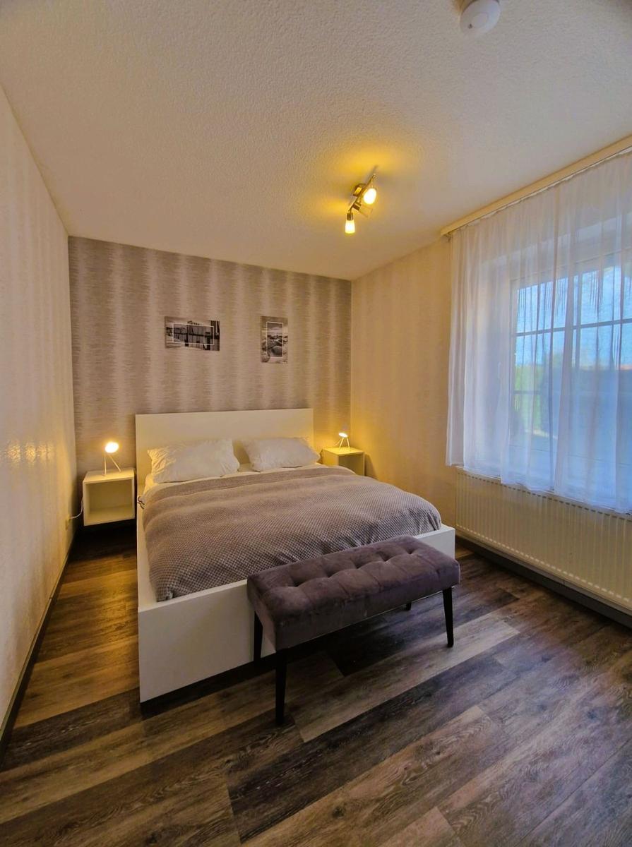 Schlafzimmer mit Bett, Nachttischen und Fenster mit Vorhängen.