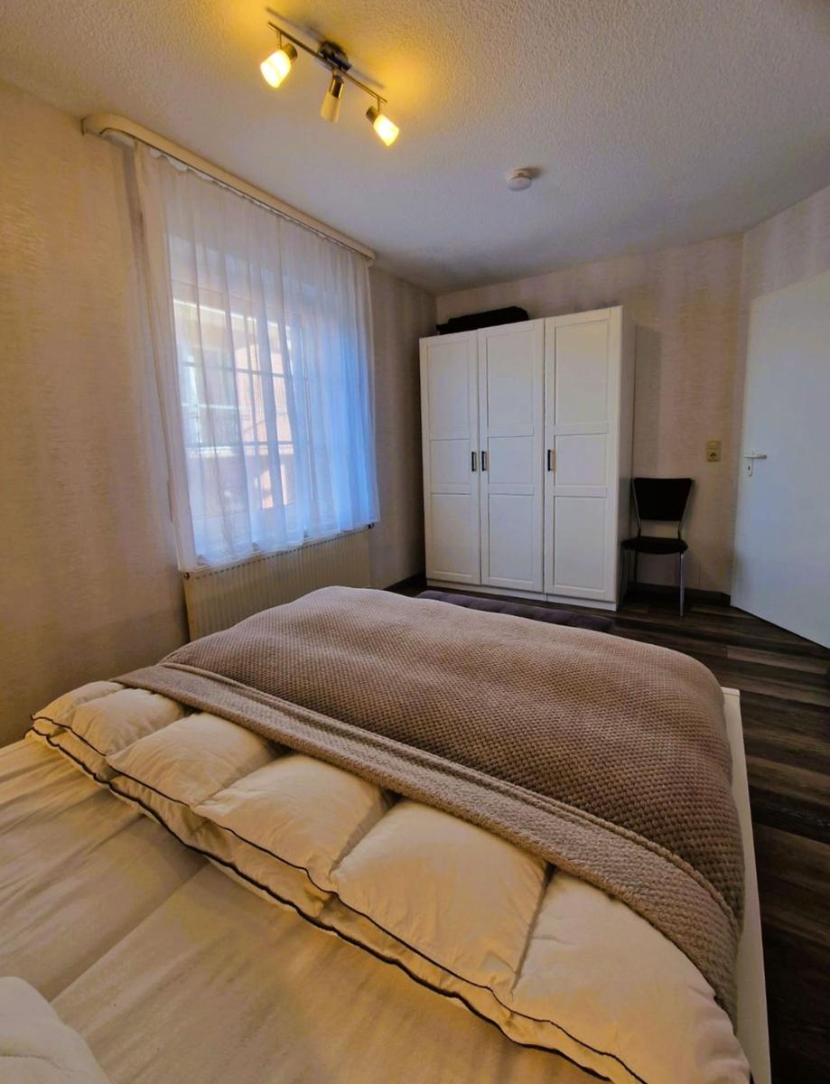 Schlafzimmer mit Bett, Kleiderschrank und Fenster mit Vorhängen.