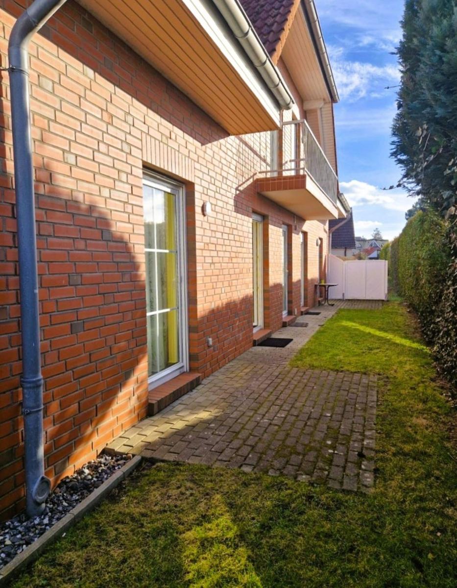 Haus mit Backsteinfassade, Balkon und gepflasterter Weg neben Grünfläche.