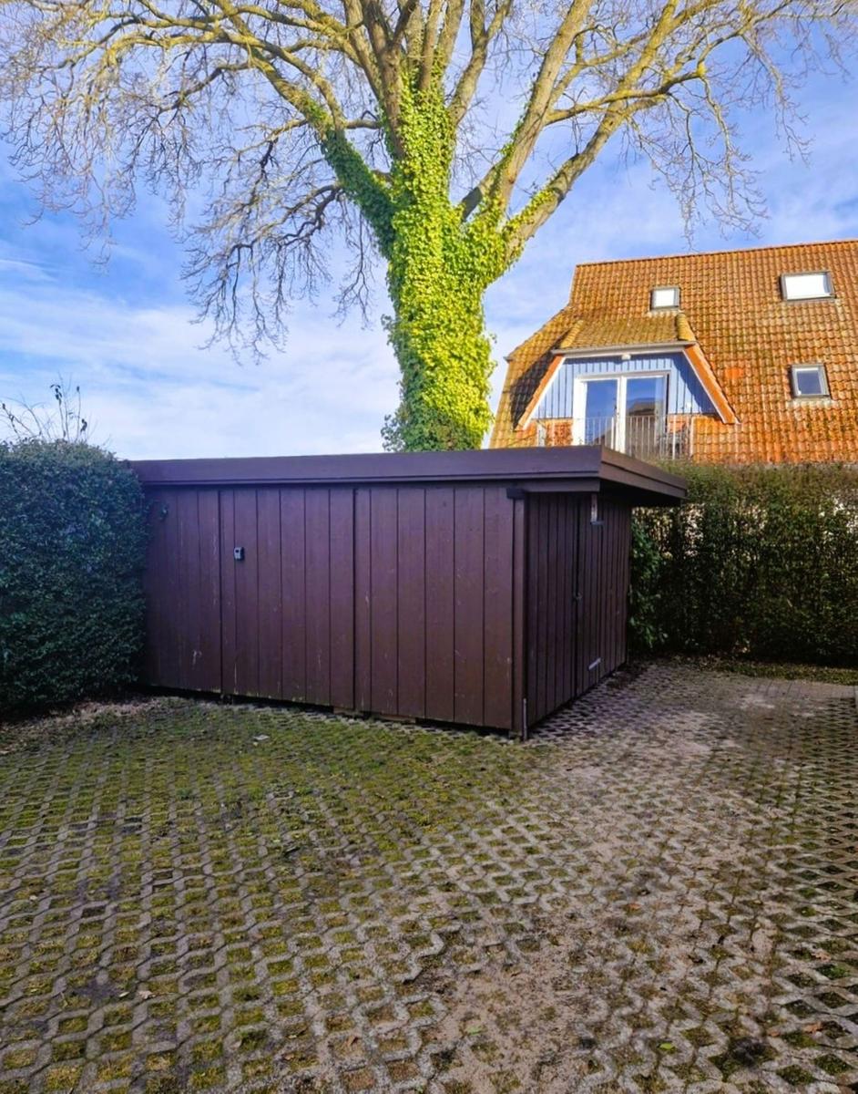 Hinterhof mit Holzgarage, großen Baum und Terrasse im Hintergrund.