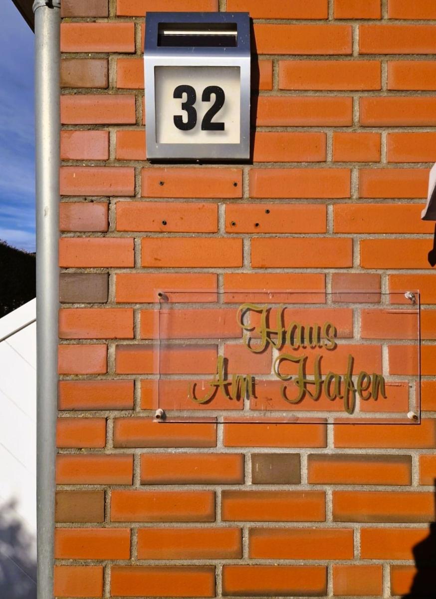 Hausnummer 32 an einer roten Ziegelwand mit Schild Haus Am Hafen.