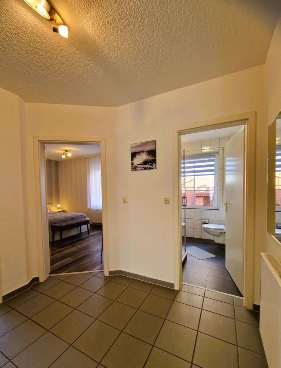Flur mit Blick in Schlafzimmer und Bad. Bodenfliesen, Wandbild und Türöffnungen sichtbar.