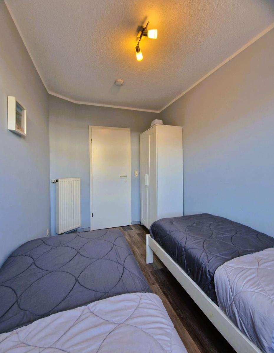 Zwei Betten mit Bettwäsche, Kleiderschrank und Heizkörper in einem Raum.