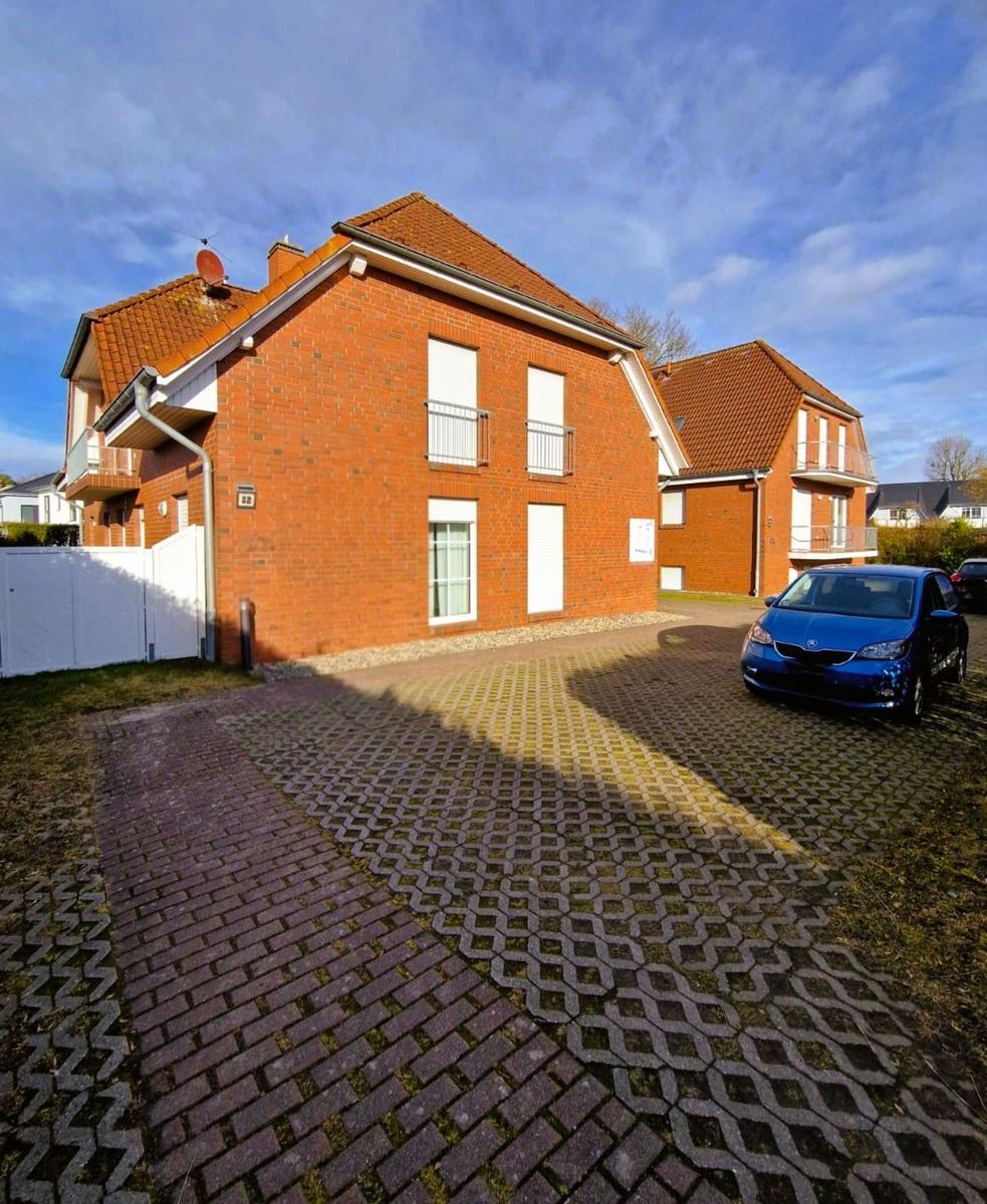 Zweistöckiges Backsteinhaus mit Balkon und gepflastertem Hof. Ein blauer Wagen steht vor dem Haus.