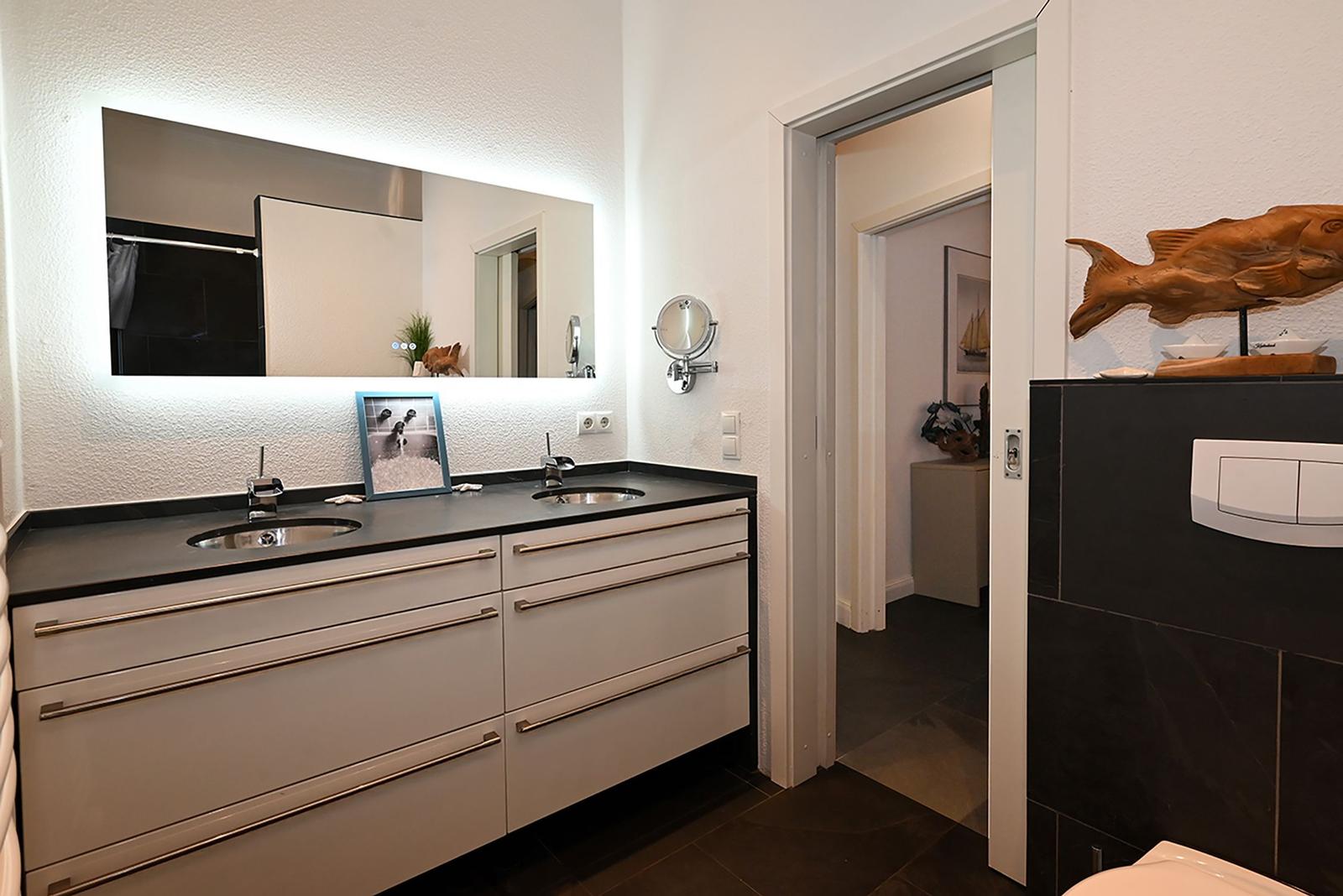 Badezimmer mit Doppelwaschbecken, beleuchtetem Spiegel und Holzdekoration.
