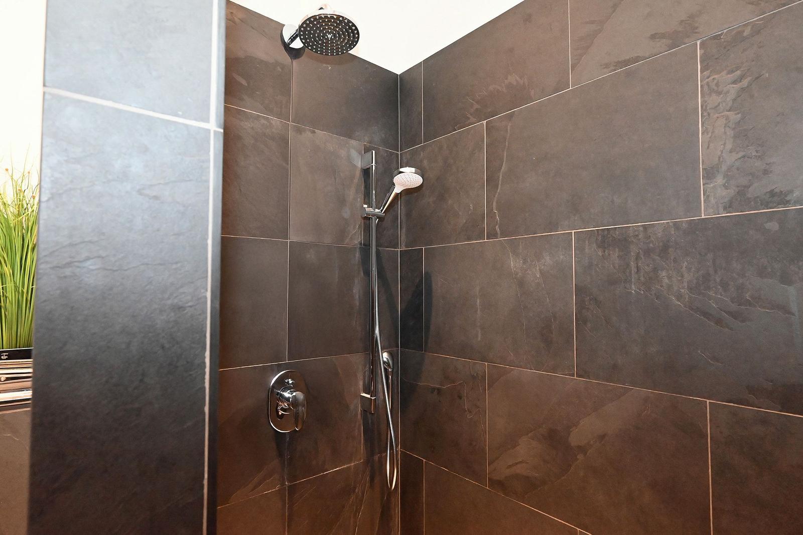 Dusche mit dunklen Fliesen und Duschkopf