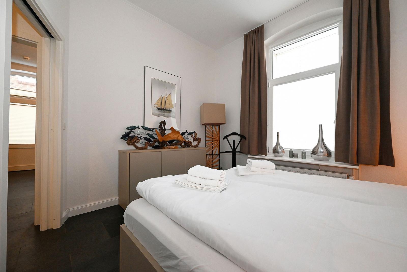 Schlafzimmer mit Bett, Fenster und dekorativen Gegenständen.