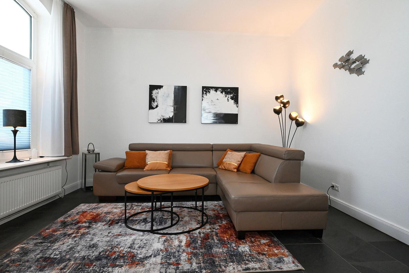 Ein Wohnzimmer mit braunem Sofa, runden Tischen und Wandbildern.