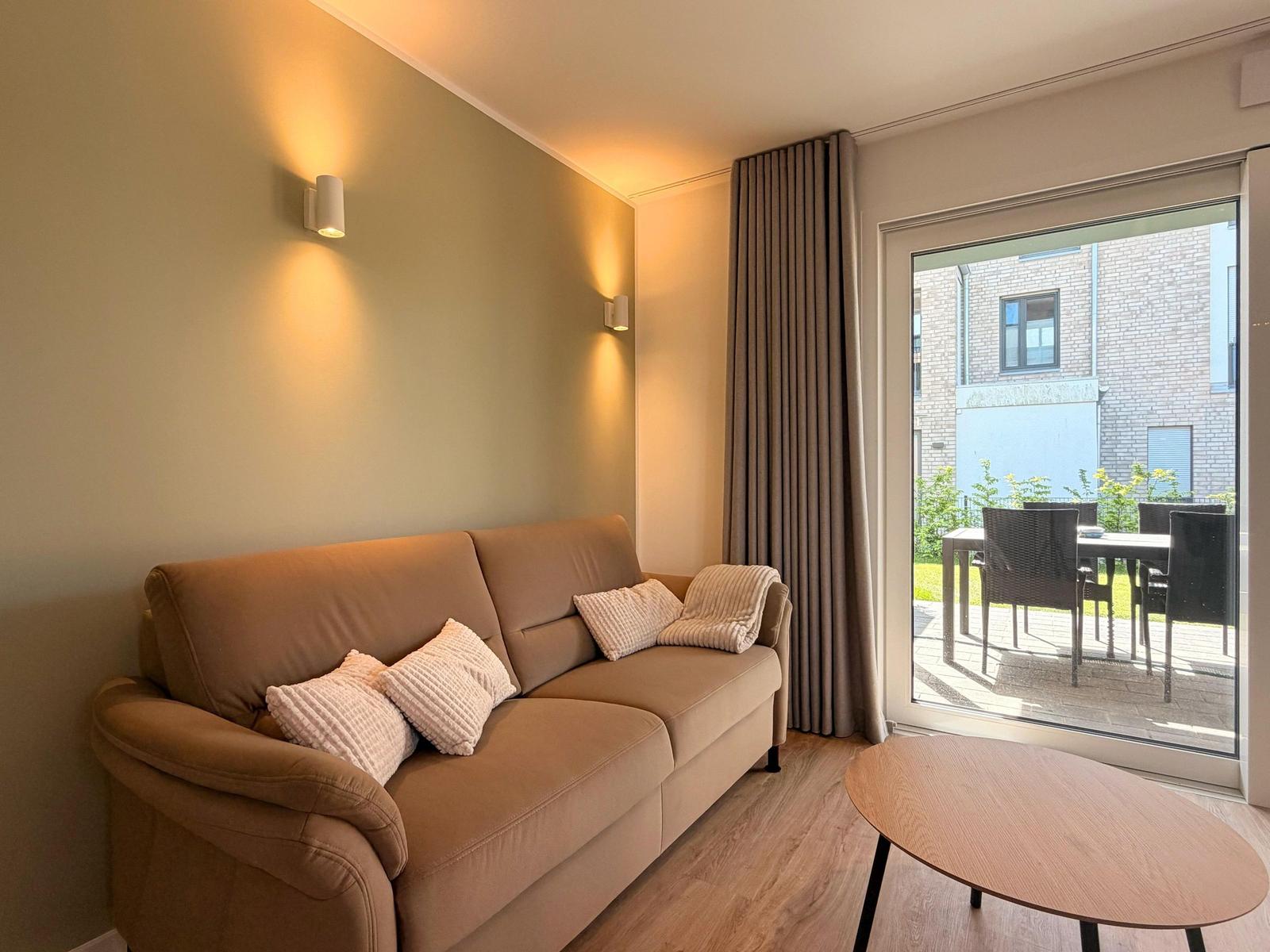Ein Sofa mit Kissen steht vor einer Glastür zum Balkon.