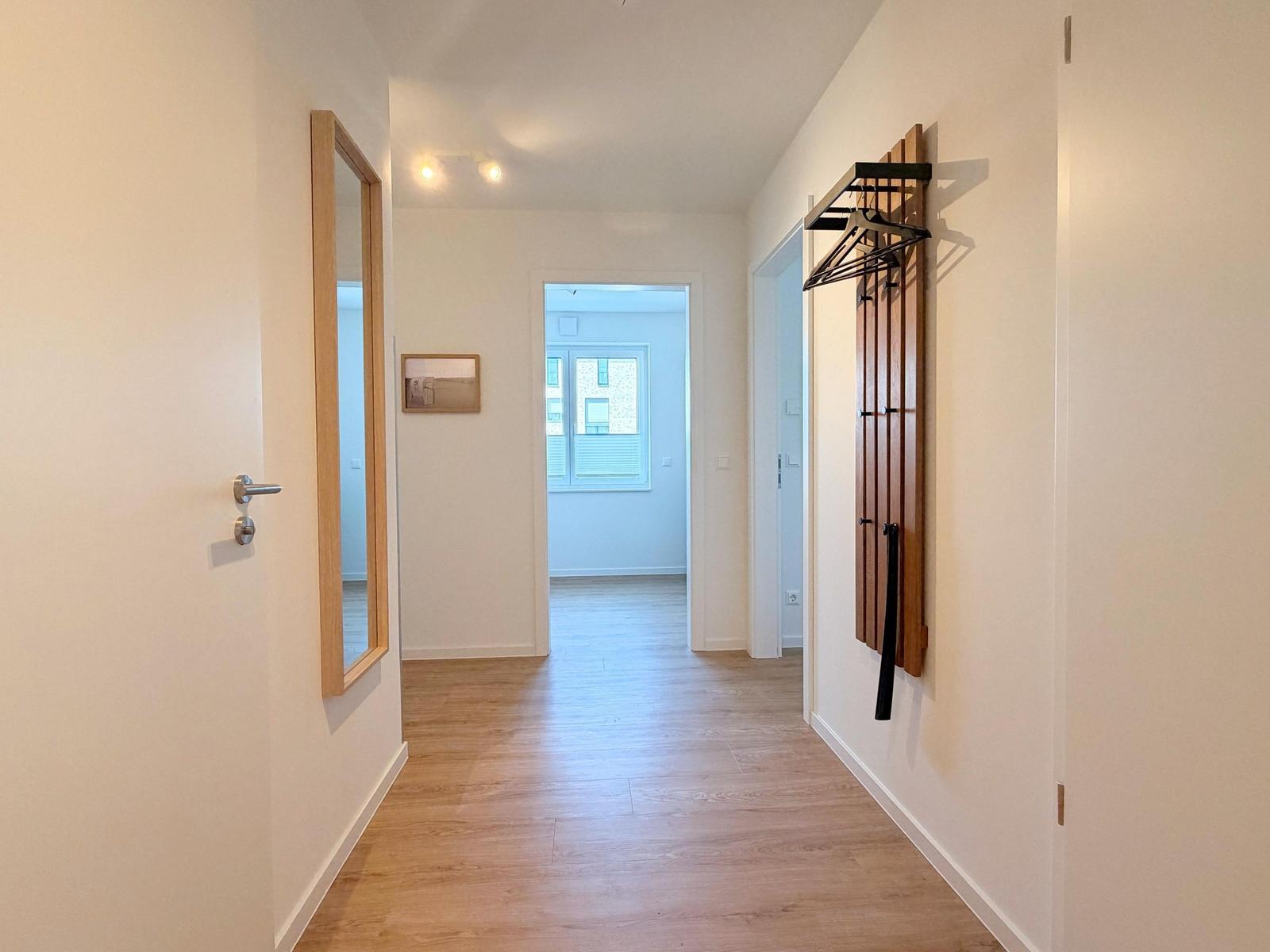 Flur mit Holzboden, Spiegel und Kleiderständer an der Wand.