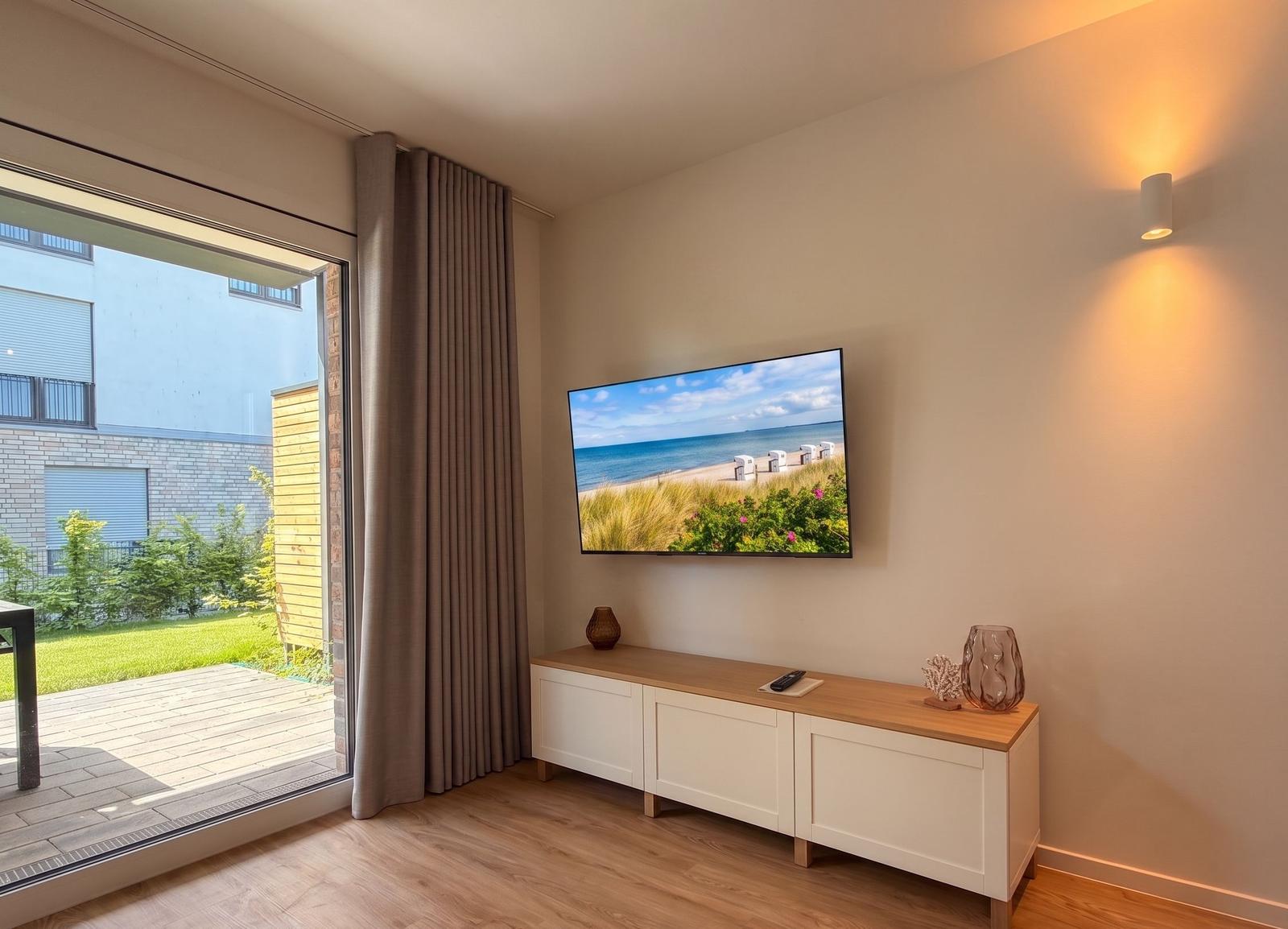 Wohnzimmer mit Fernseher und Terrassentür. Fernseher zeigt Strandbild.