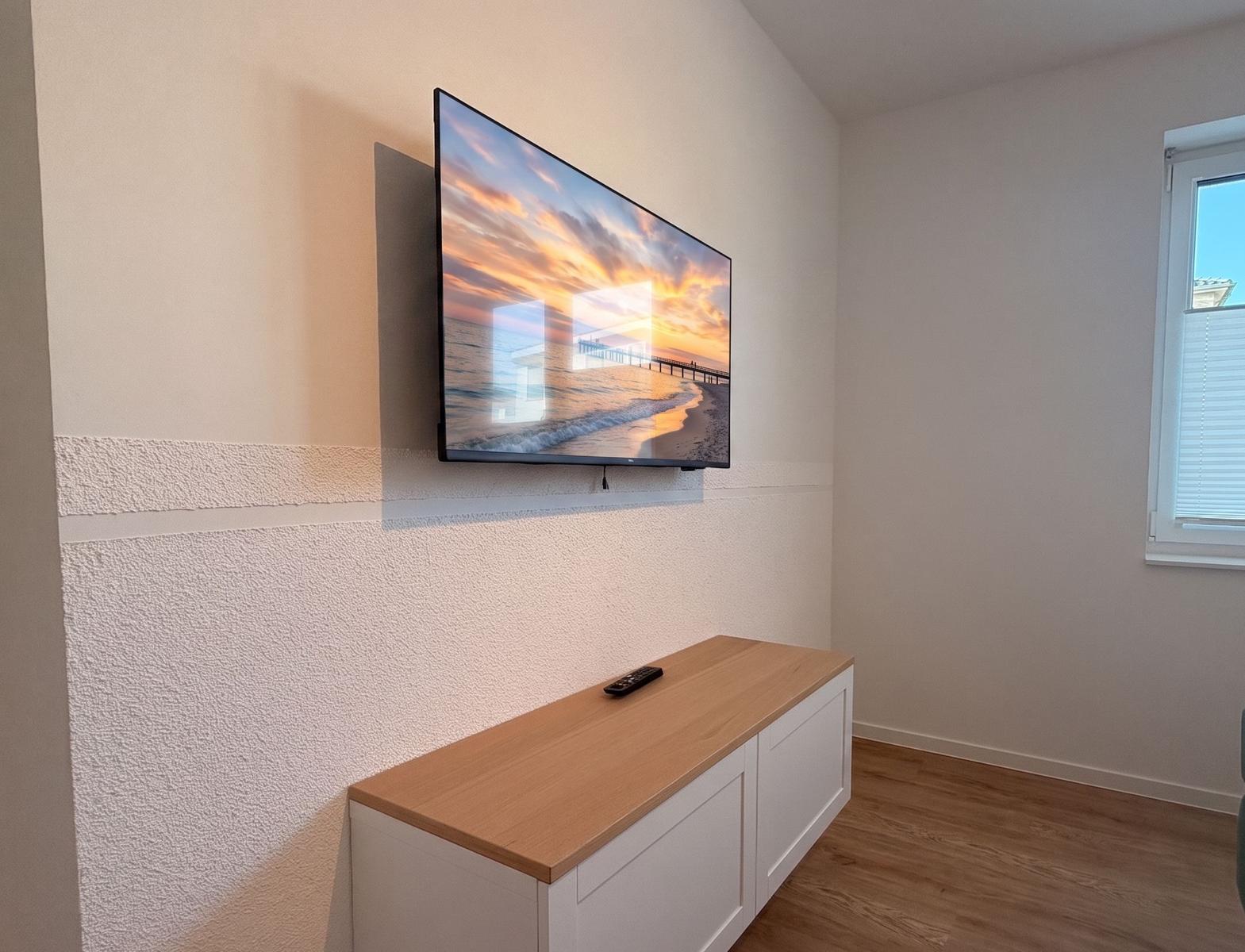 Flachbild-TV an der Wand über einem weißen Schrank mit Holzoberfläche.