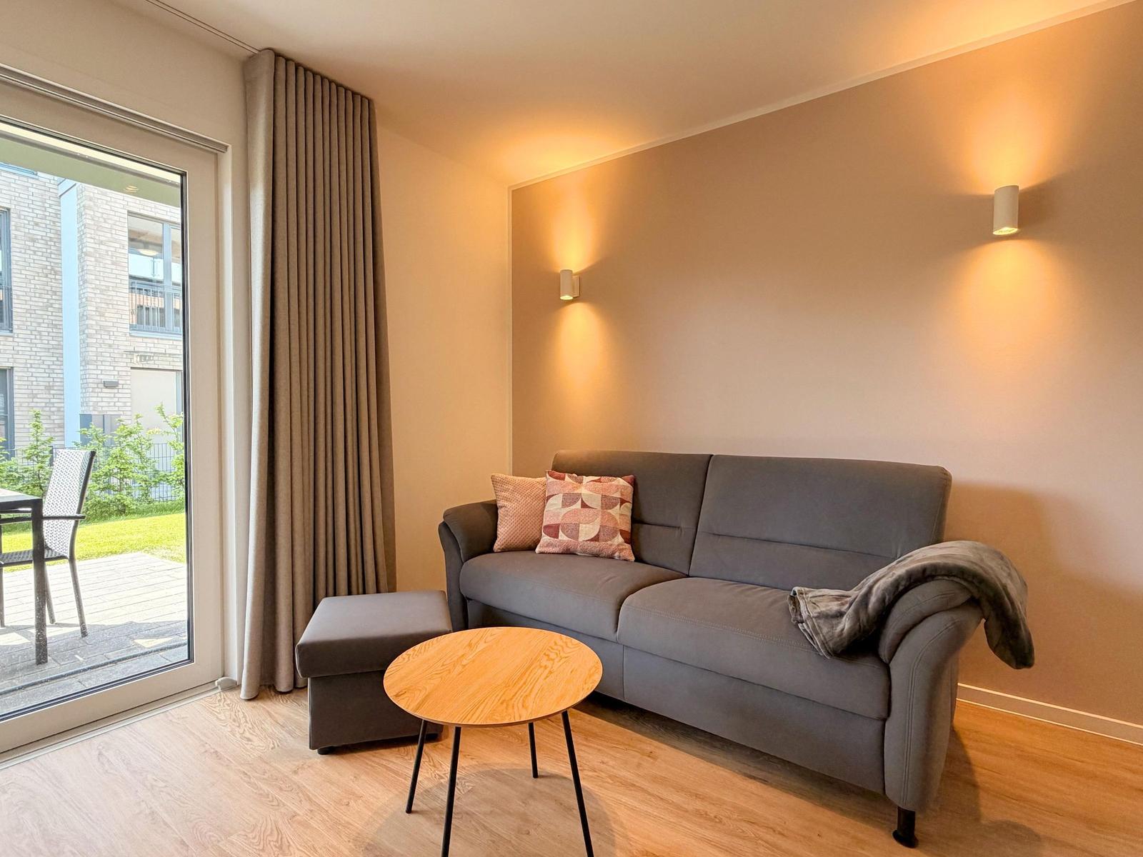 Ein Wohnzimmer mit grauem Sofa, runden Tisch und Blick auf Balkon.