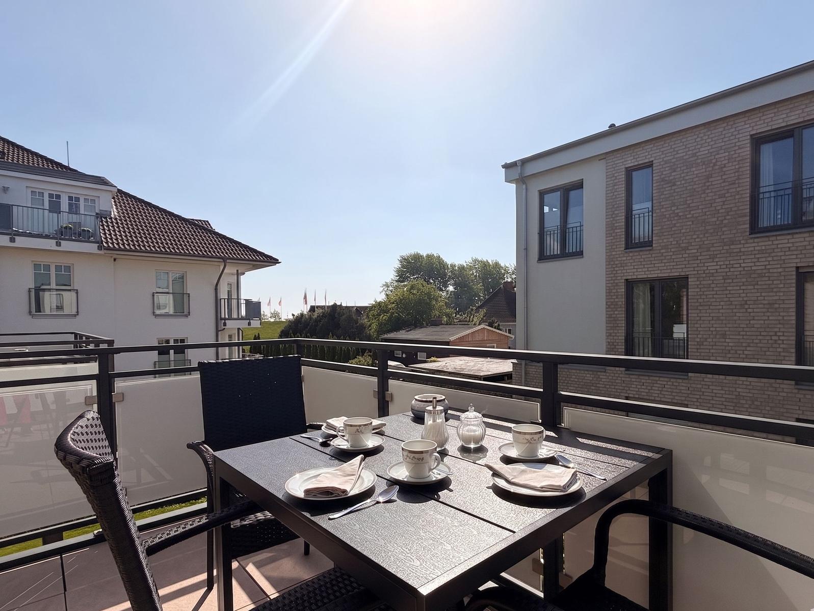 Terrasse mit Tisch und Stühlen für vier Personen, Blick auf Wohnhäuser und Bäume.