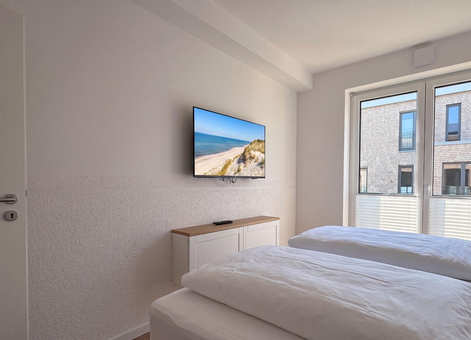 Zimmer mit zwei Betten, TV und Fenster mit Blick auf Gebäude.