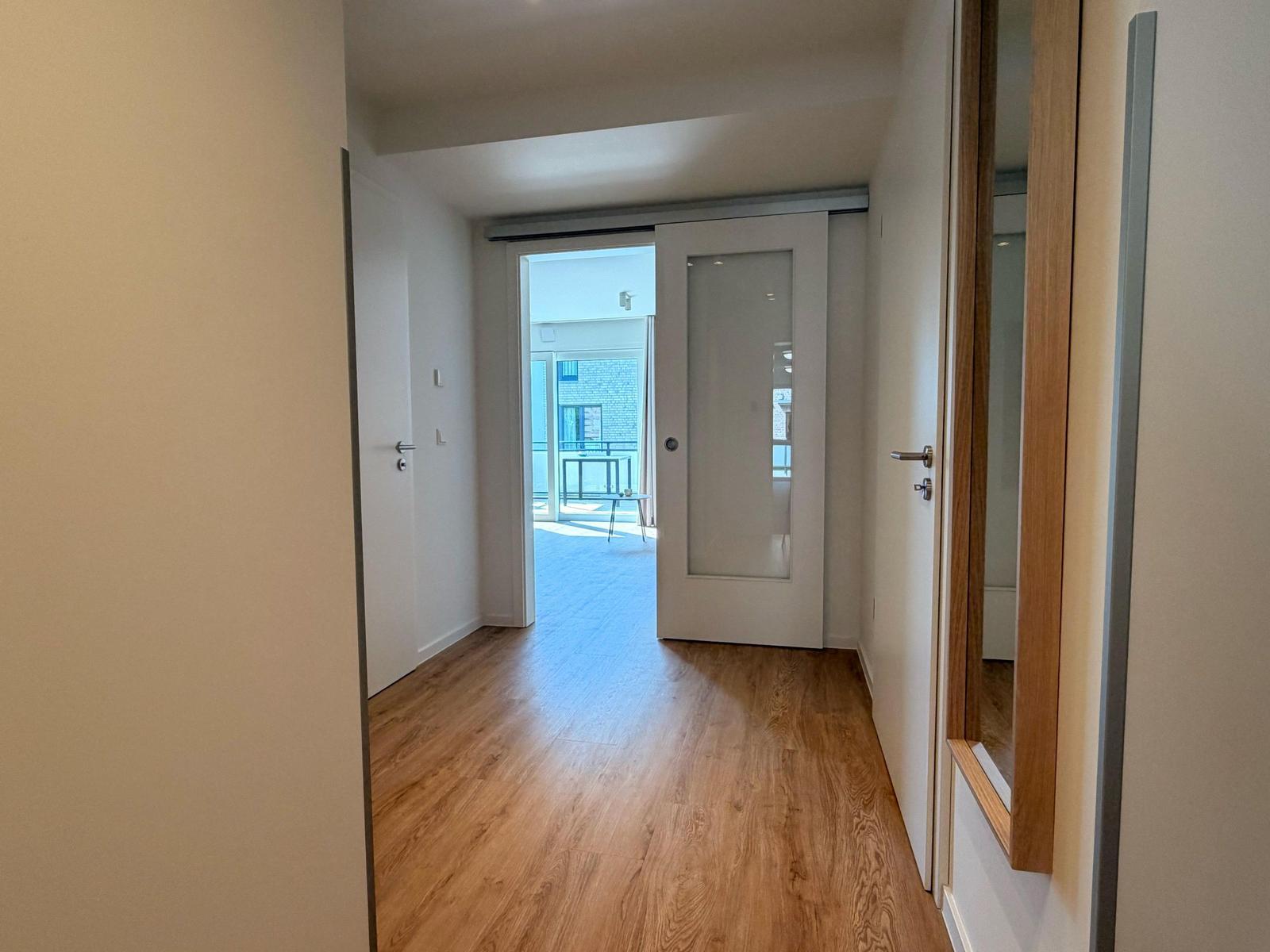 Flur mit Holzboden und Tür zu Balkon. Spiegel und Türen sichtbar.