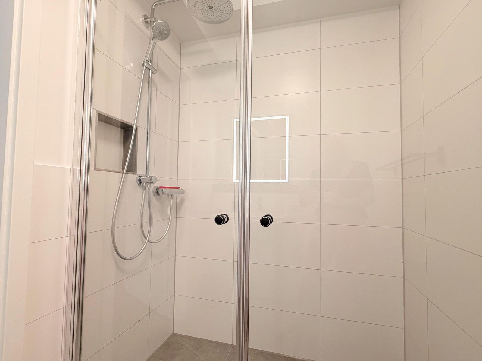 Dusche mit Glaswand, Duschbrause und eingebautem Spiegel