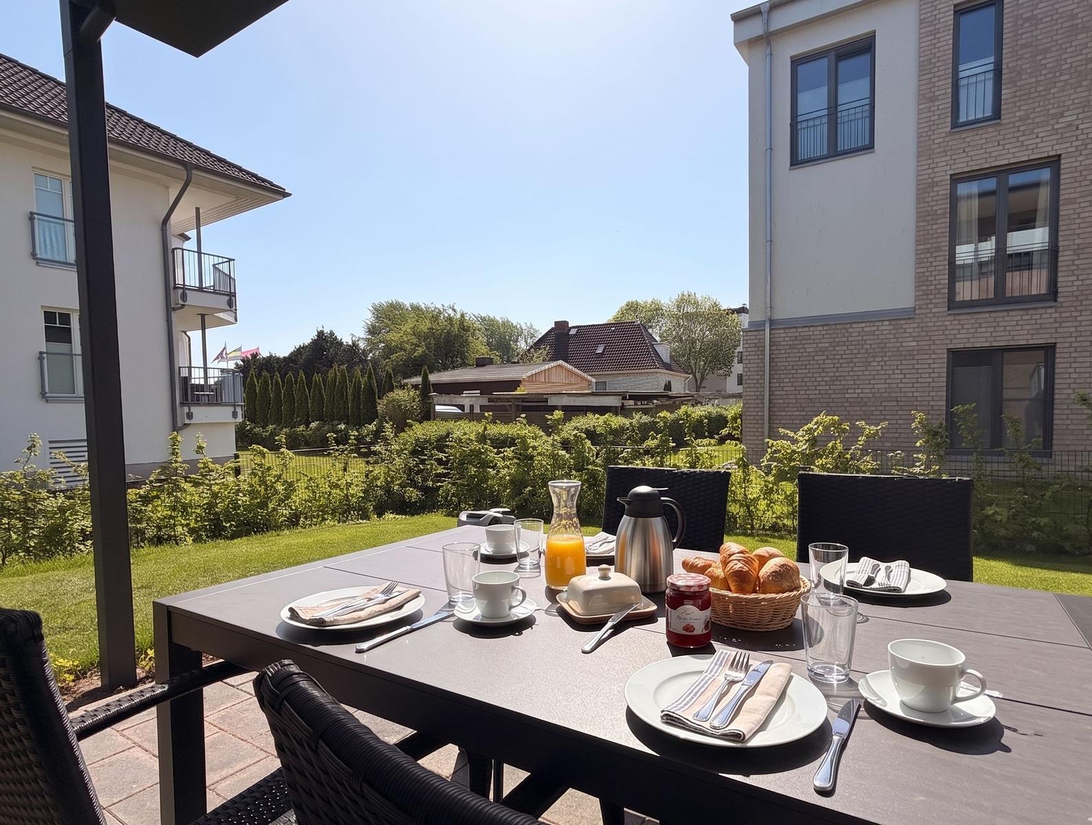 Garten-Terrasse mit gedecktem Frühstückstisch und Blick auf Wohnhäuser.