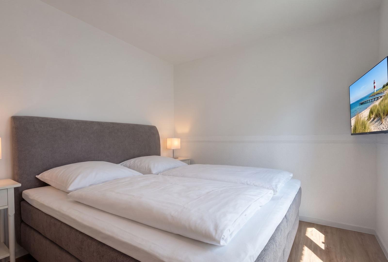 Schlafzimmer mit Doppelbett, Nachttisch und Wandbildschirm.