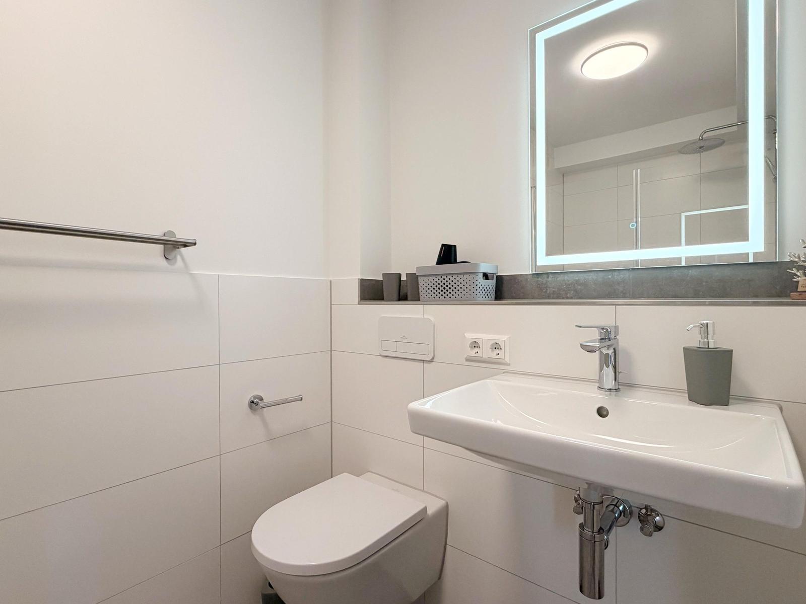 Badezimmer mit Toilette, Waschbecken und beleuchtetem Spiegel.