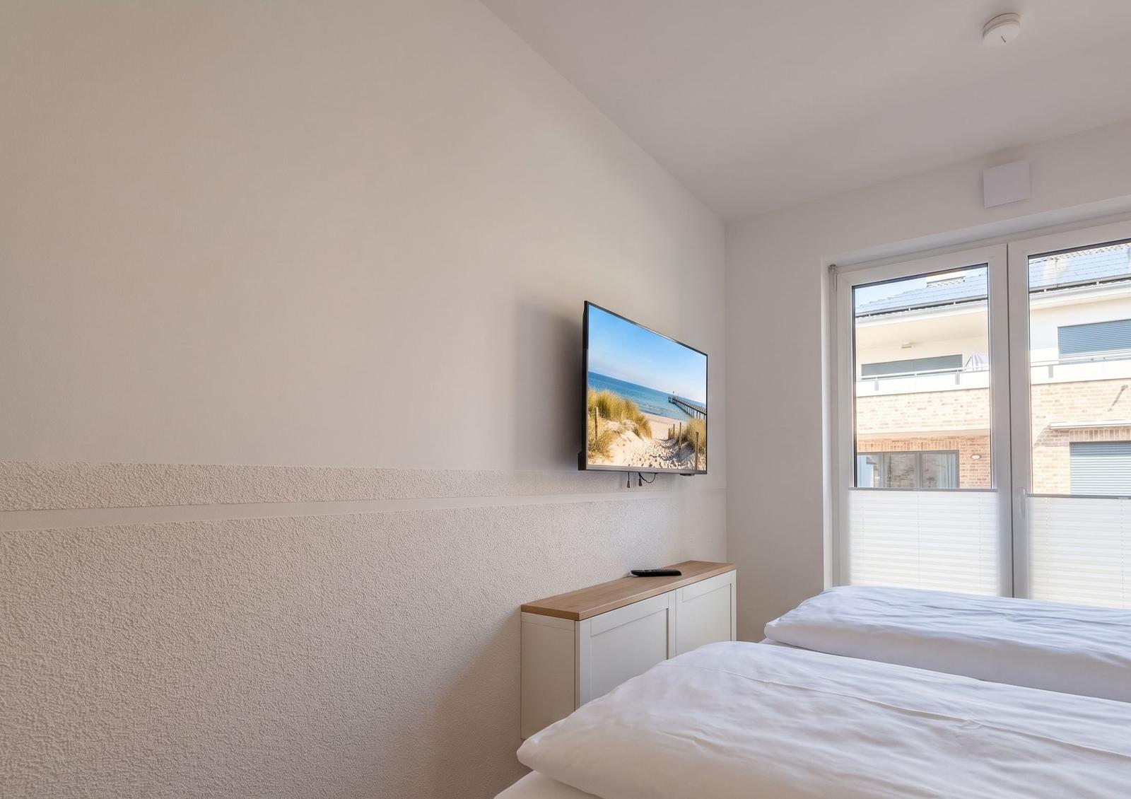 Schlafzimmer mit Bett, Fernseher und Fenster.