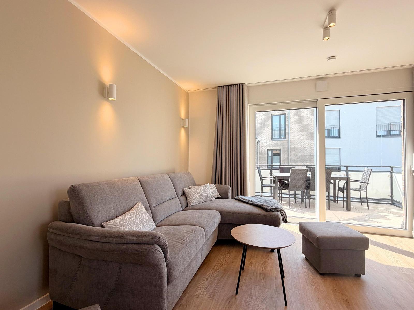 Wohnzimmer mit Sofa, Couchtisch und Blick auf Balkon mit Tisch und Stühlen.