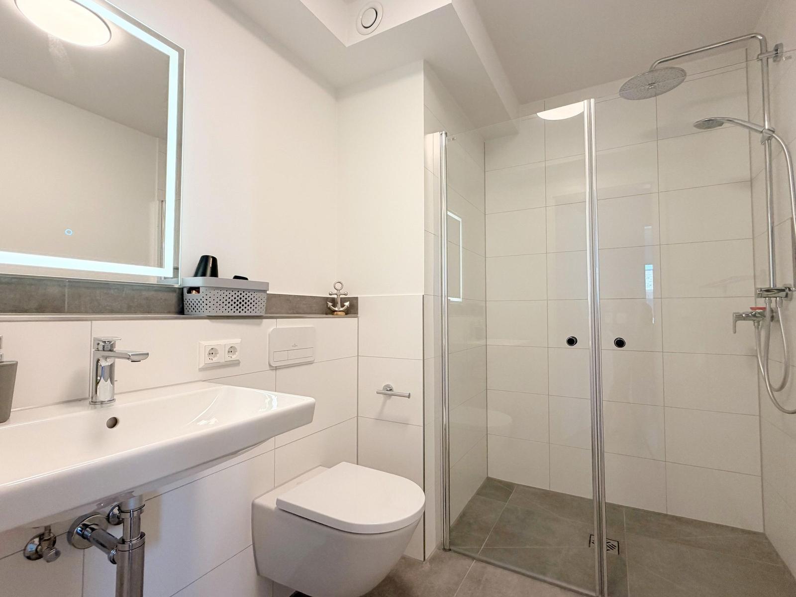 Bad mit Dusche, Waschbecken und Toilette. Spiegel mit Beleuchtung und Anker-Dekoration.