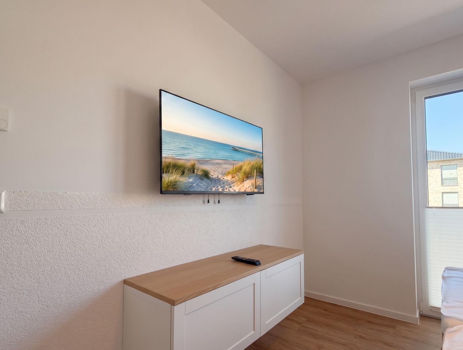 TV an der Wand über einem weißen Schrank mit Holzoberfläche.