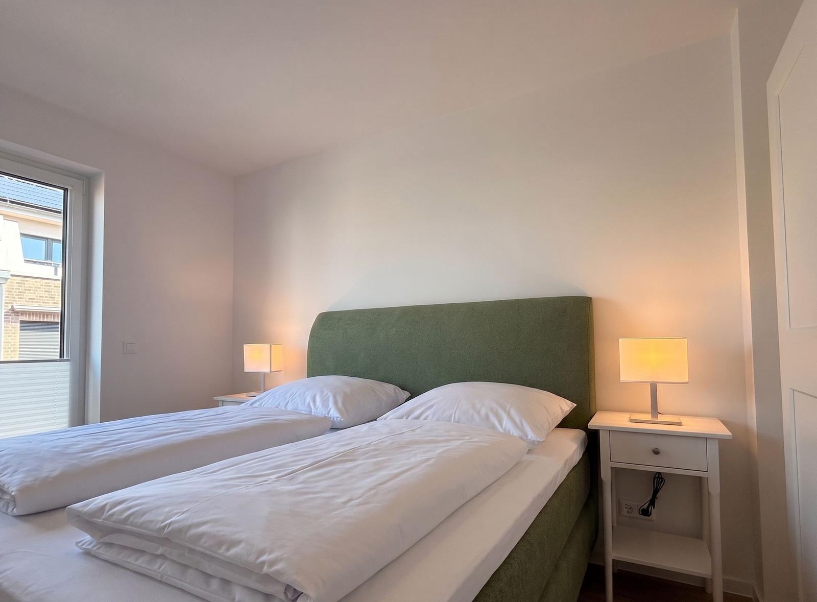 Schlafzimmer mit Doppelbett, grünem Kopfteil und zwei Nachttischen mit Lampen.