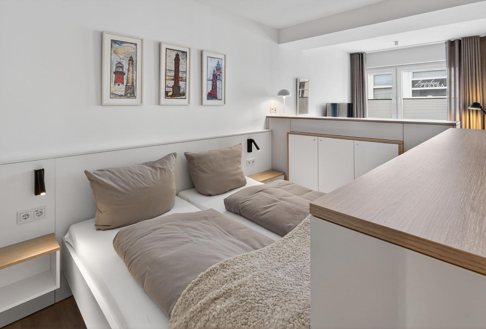 Zimmer mit Doppelbett, drei Bildern an der Wand und Fenster mit Vorhängen.