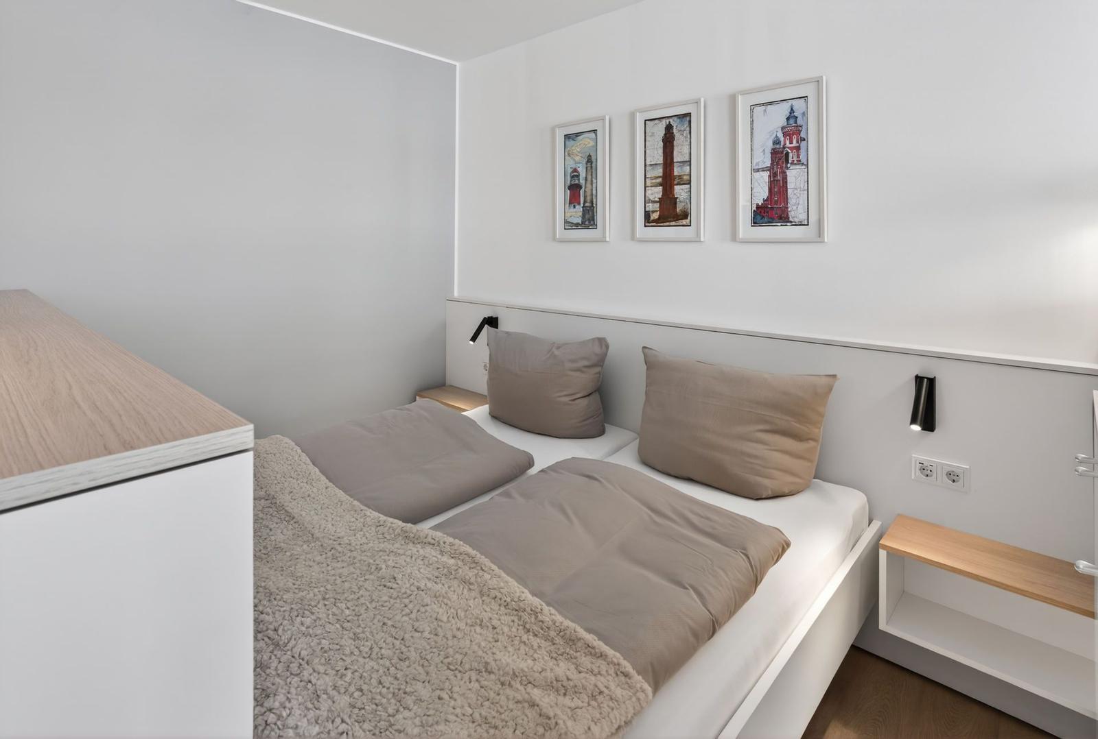 Schlafzimmer mit Bett, Nachttischen und Wandbildern von Leuchttürmen.
