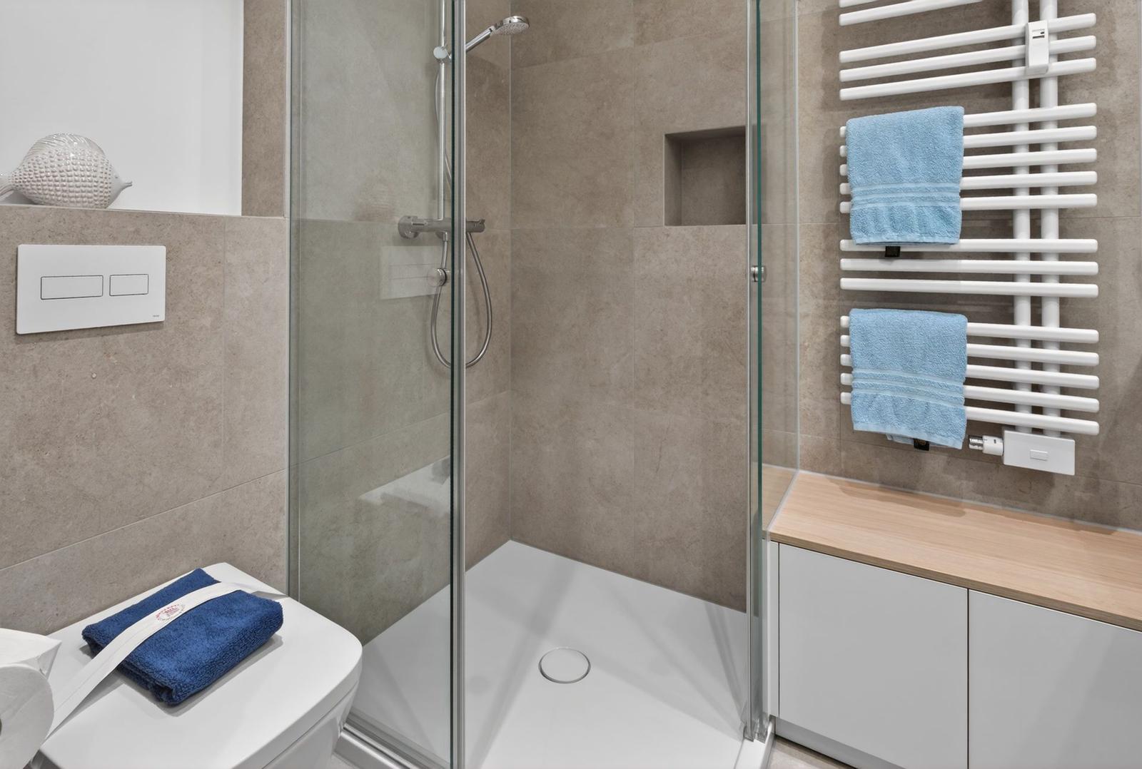 Dusche mit Glaswand, Heizkörper und Toilette mit Handtuch.
