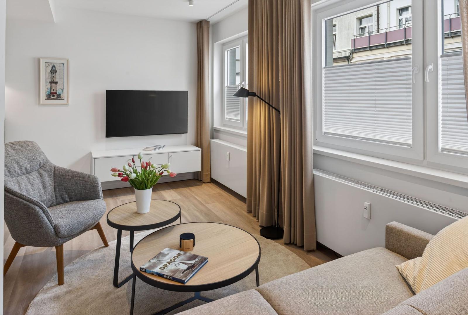 Wohnzimmer mit Sofa, Sessel, TV und Fenster mit Jalousien.