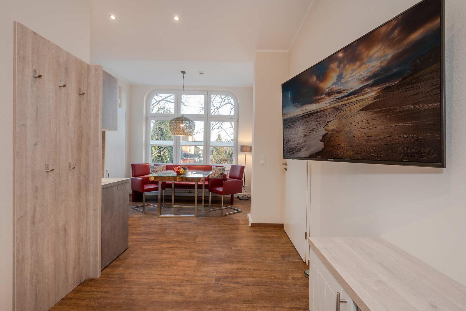 Wohnbereich mit Essbereich, rotem Sofa und großen Fenstern. Wandbild und Holzboden.