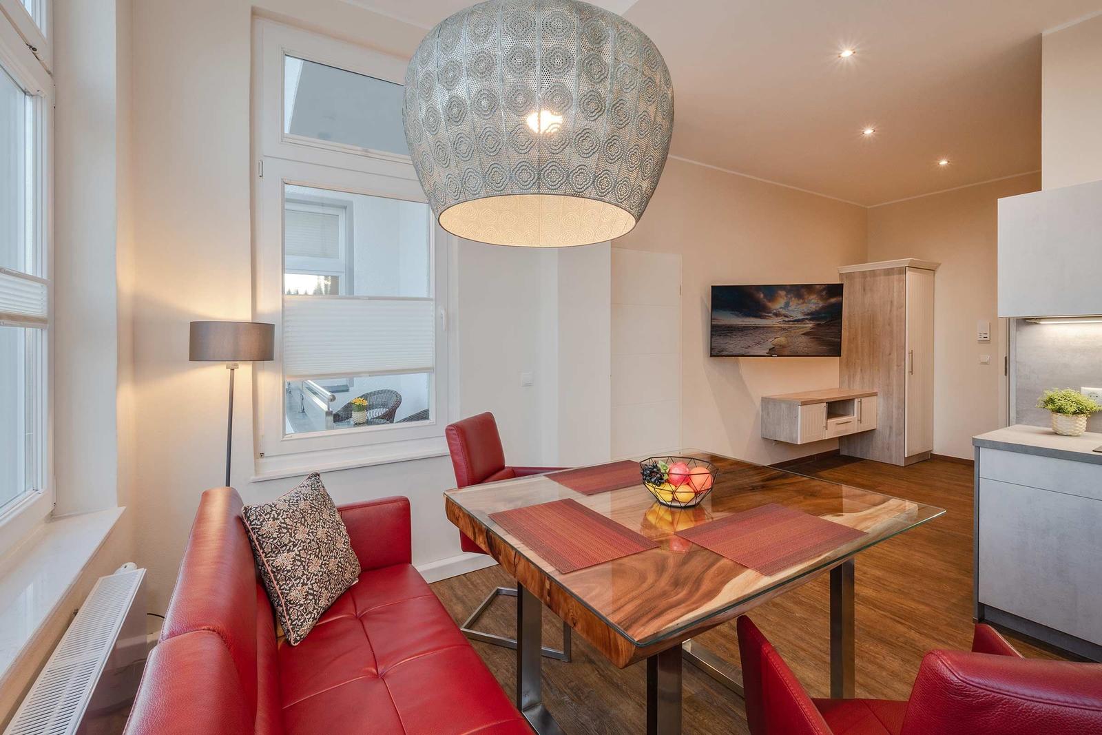 Ein Essbereich mit rotem Sofa, Glas-Tisch und moderner Deckenleuchte.