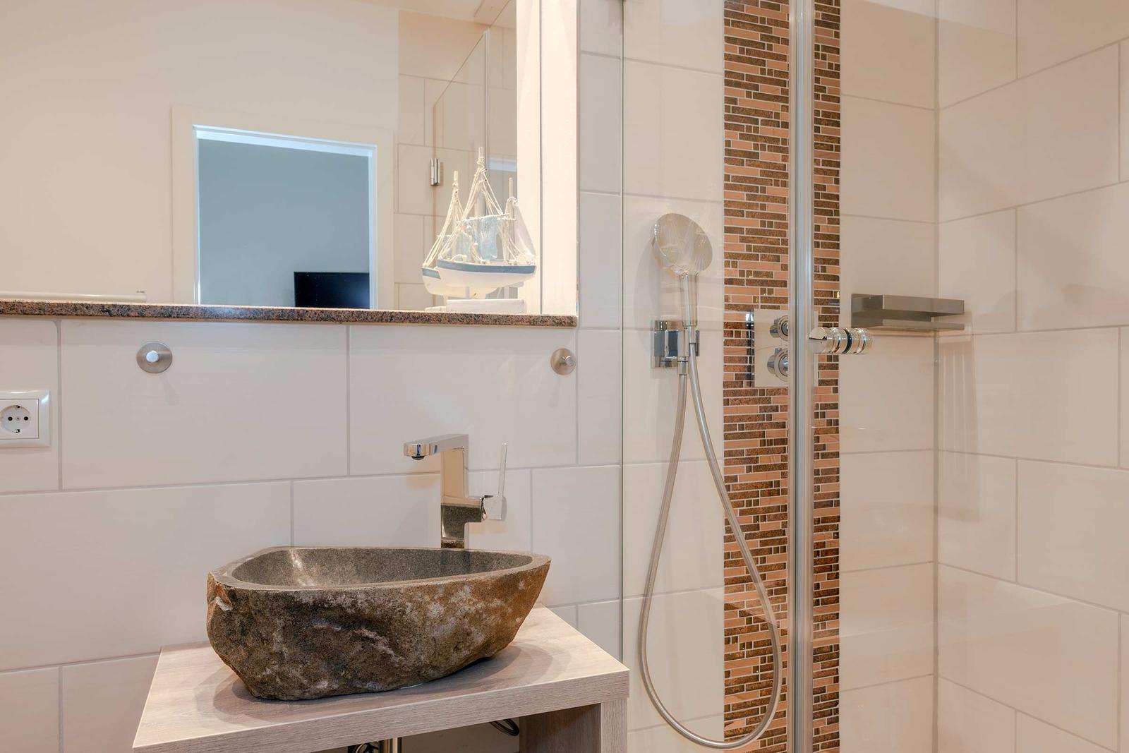 Bad mit Steinwaschbecken, Dusche und Spiegel mit Segelbootdekoration.