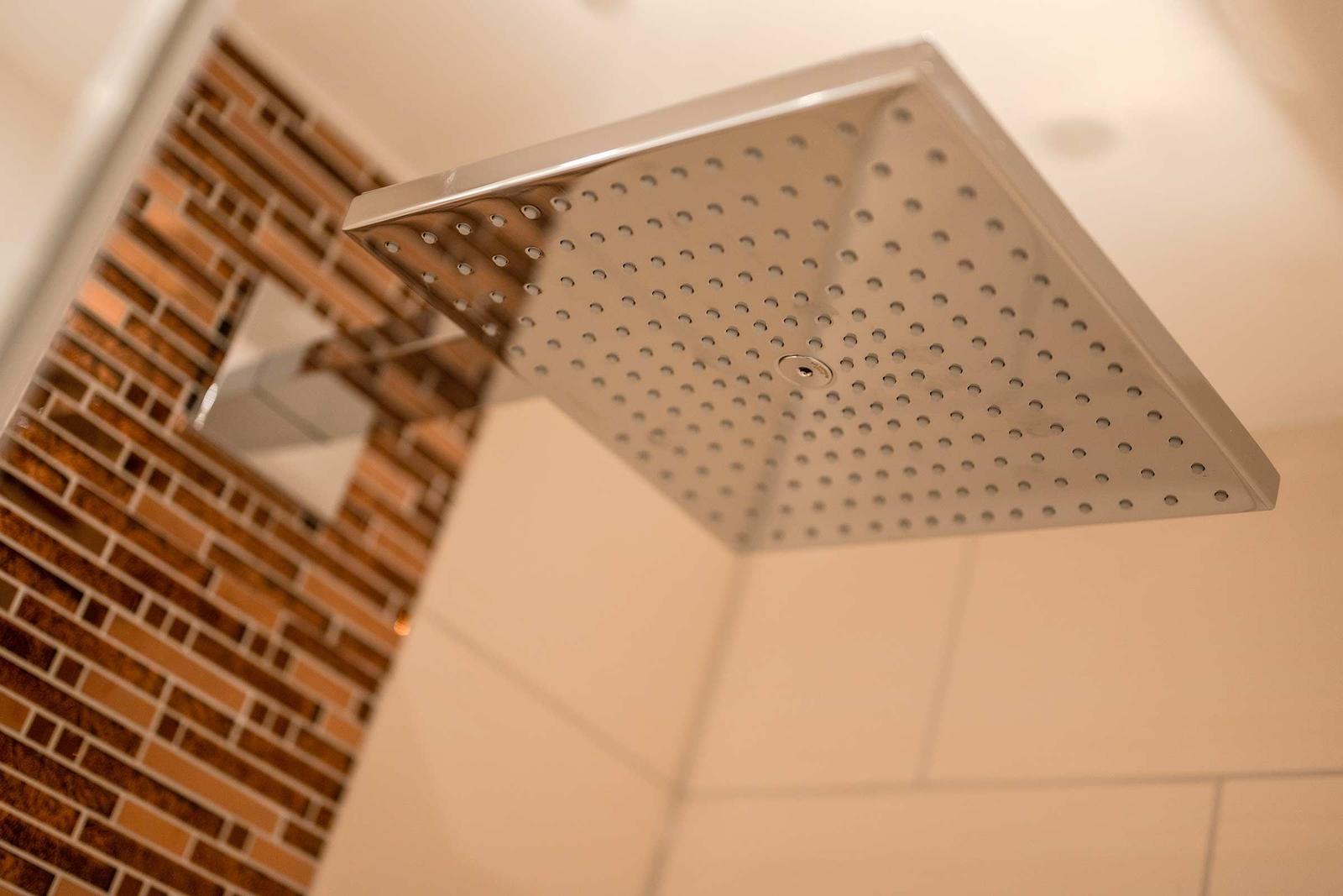 Große Duschkopf mit mehreren Düsen und Mosaikfliesen an der Wand.