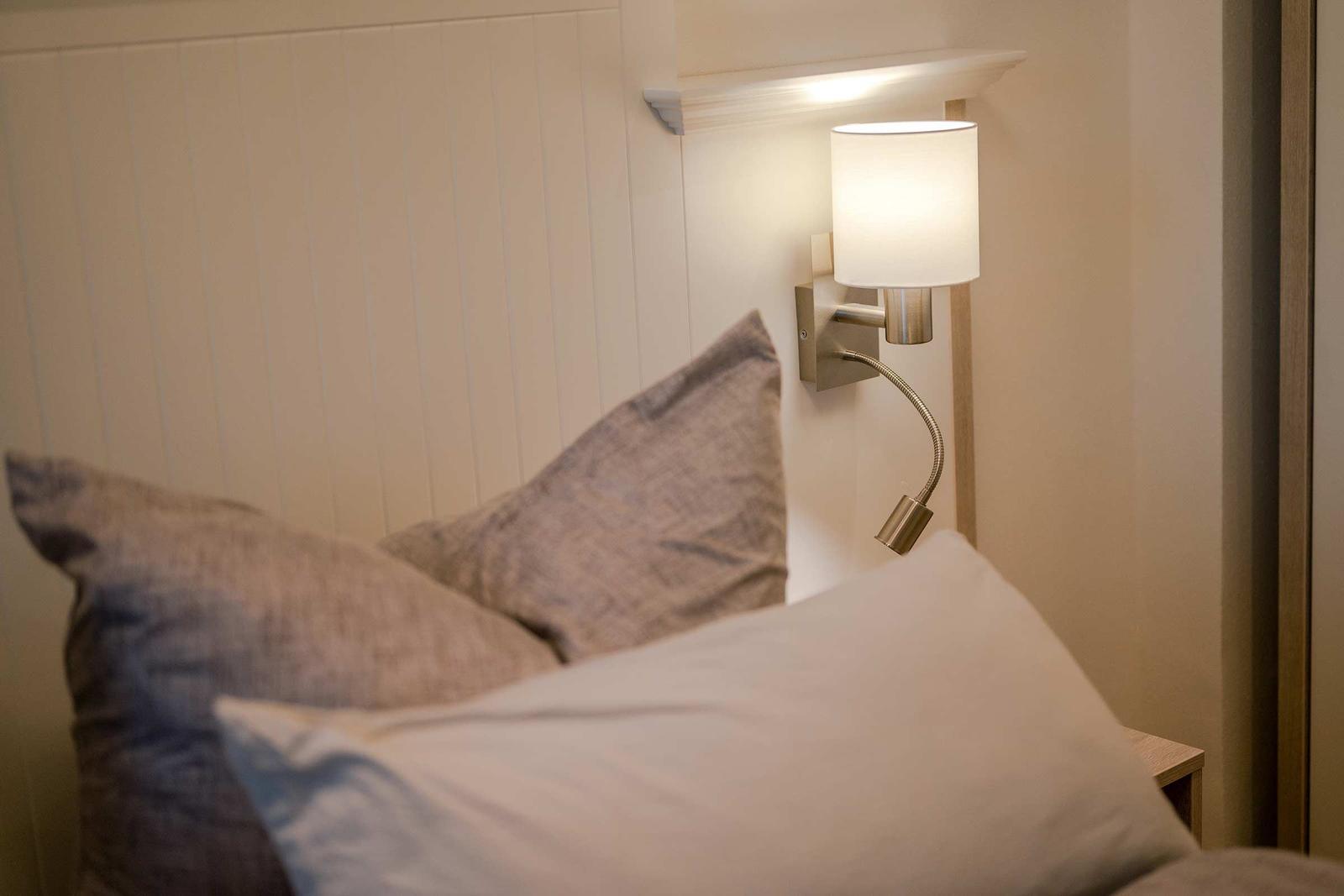 Bettkopfteil mit Kissen und Wandlampe mit Schwenkarm.