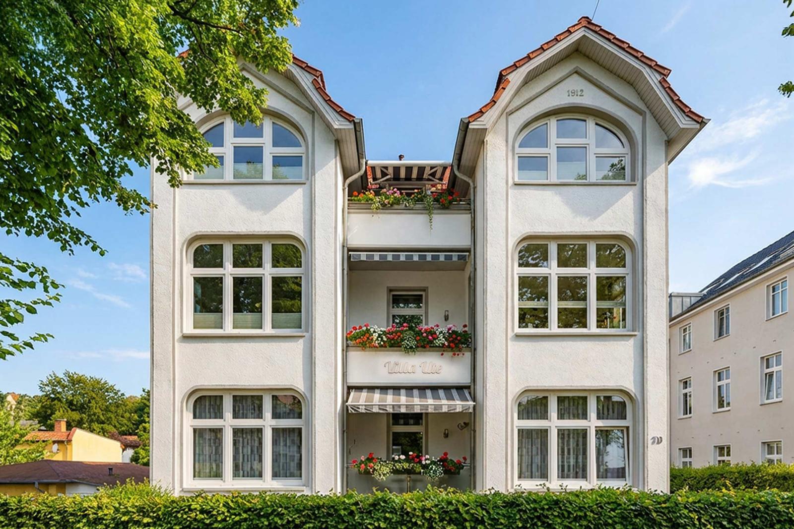 Weiße Villa mit rotem Dach und Blumenboxen an Balkonen. Baujahr 1912.