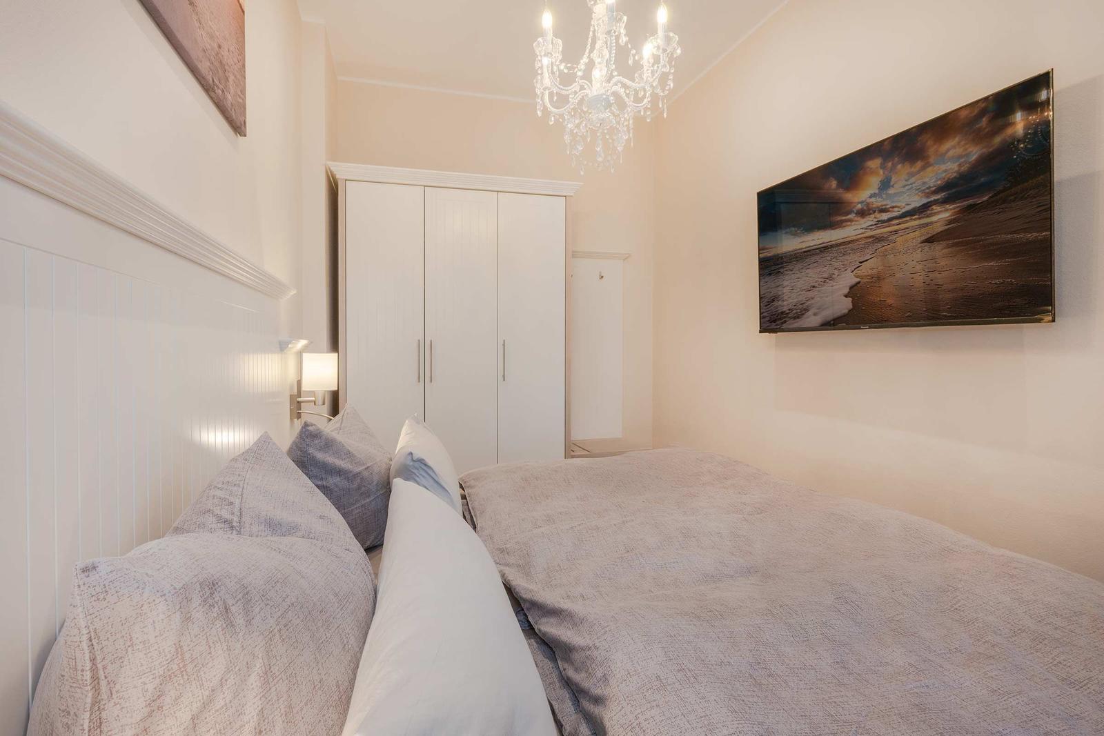Schlafzimmer mit Bett, Kleiderschrank und Wandbild. Deckenleuchte und Wandlampe.