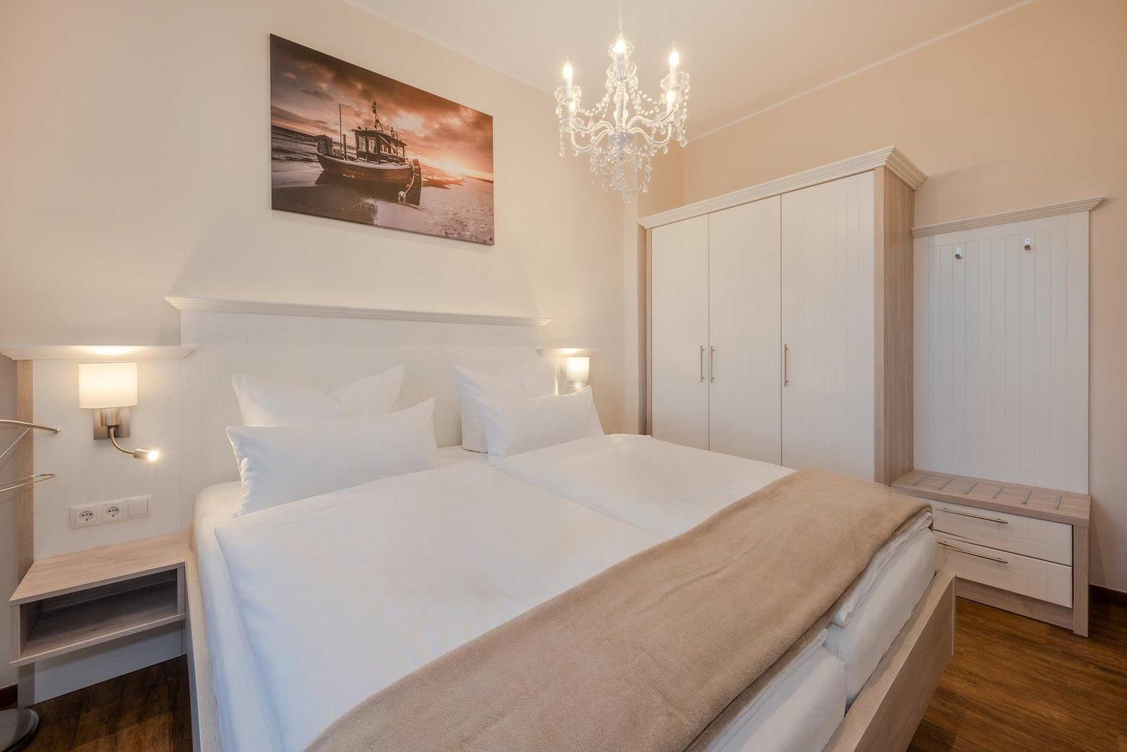 Doppelbett mit weißer Bettwäsche, Schrank und Wandbild mit Boot.