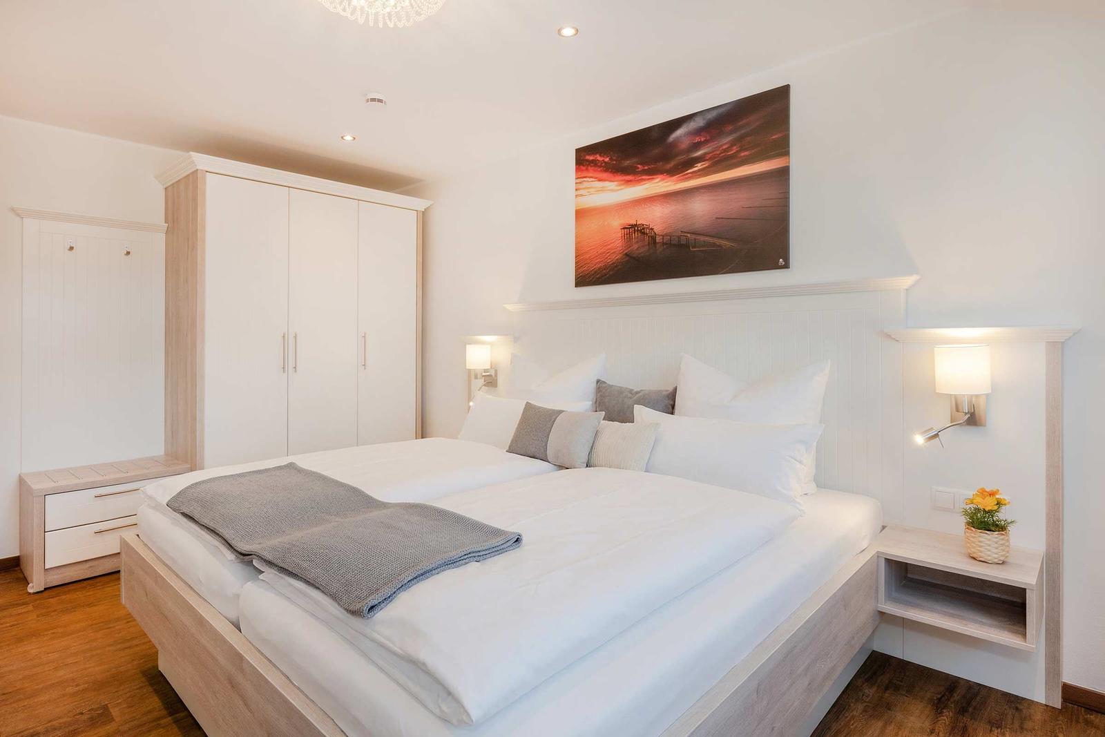 Schlafzimmer mit Doppelbett, Kleiderschrank und Wandbild.