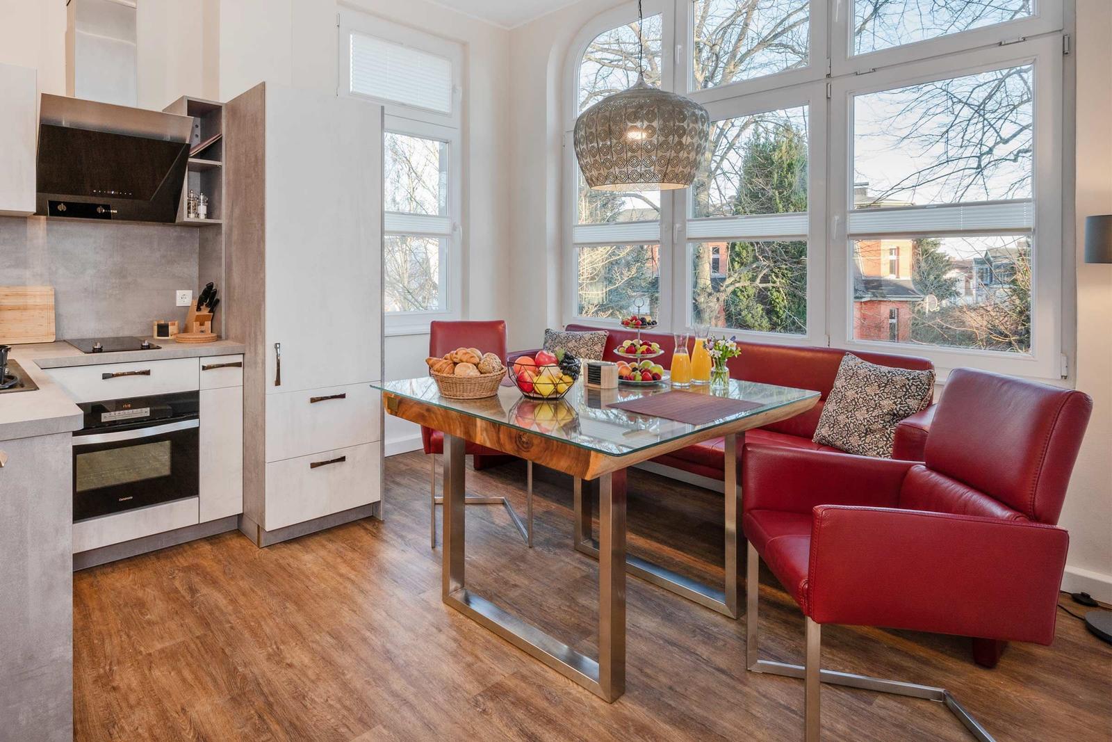 Küche und Essbereich mit rotem Sofa und Glas-Tisch. Große Fenster mit Blick auf Außenbereich.