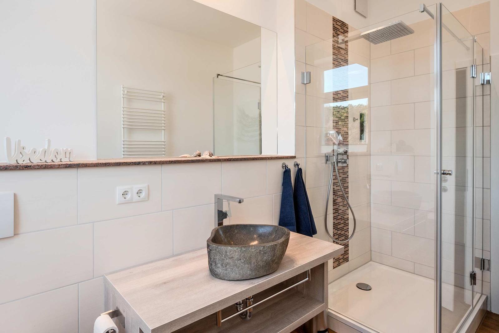 Bad mit Dusche, Waschtisch und Spiegel. Wand mit Fliesen und Handtuchhalter.