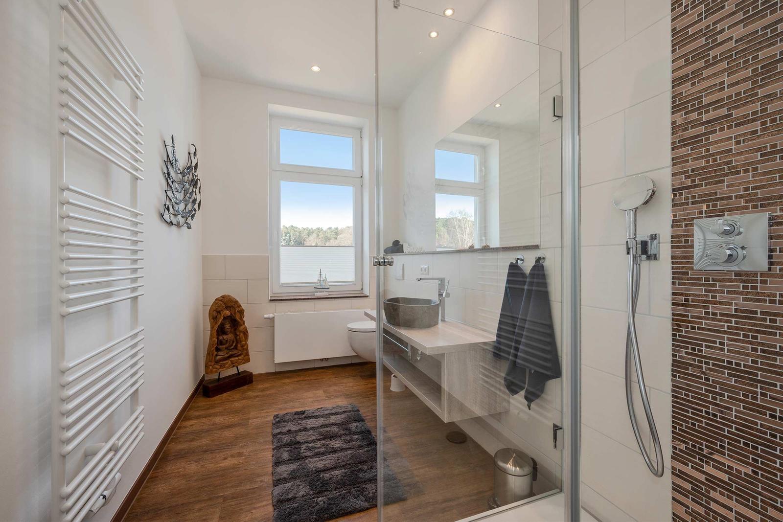 Badezimmer mit Dusche, Waschtisch und Fenster mit Blick auf die Landschaft.