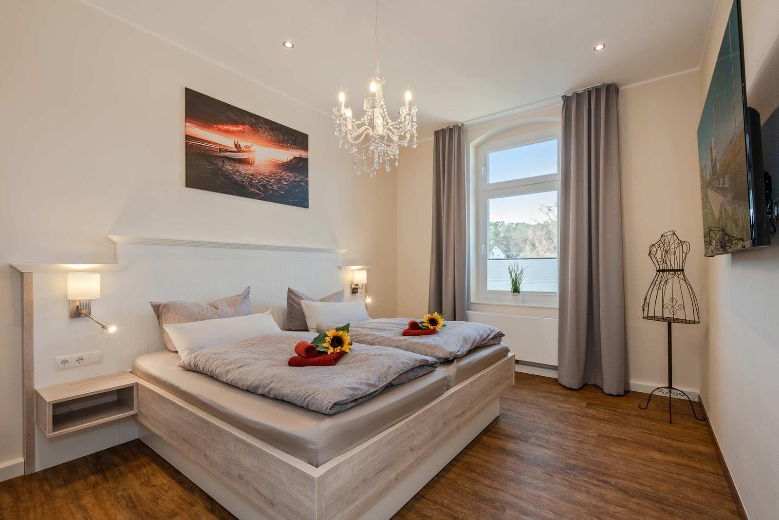 Schlafzimmer mit Doppelbett, Fenster, Vorhängen und Deckenleuchte.