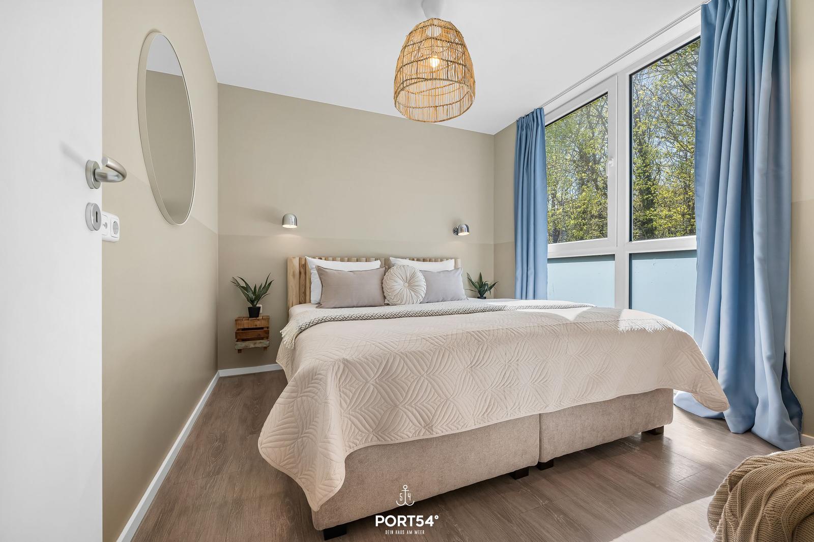 Schlafzimmer mit Bett, Fenster und blauen Vorhängen.