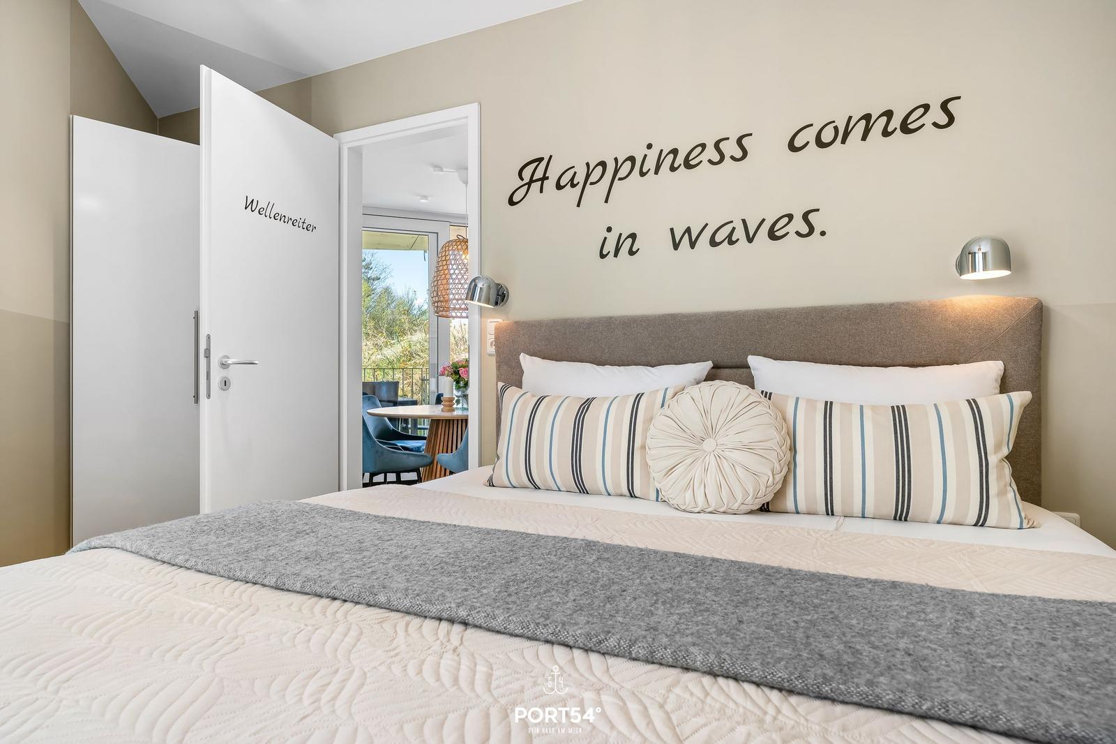 Schlafzimmer mit Bett, Wandtext und Blick auf Balkon.