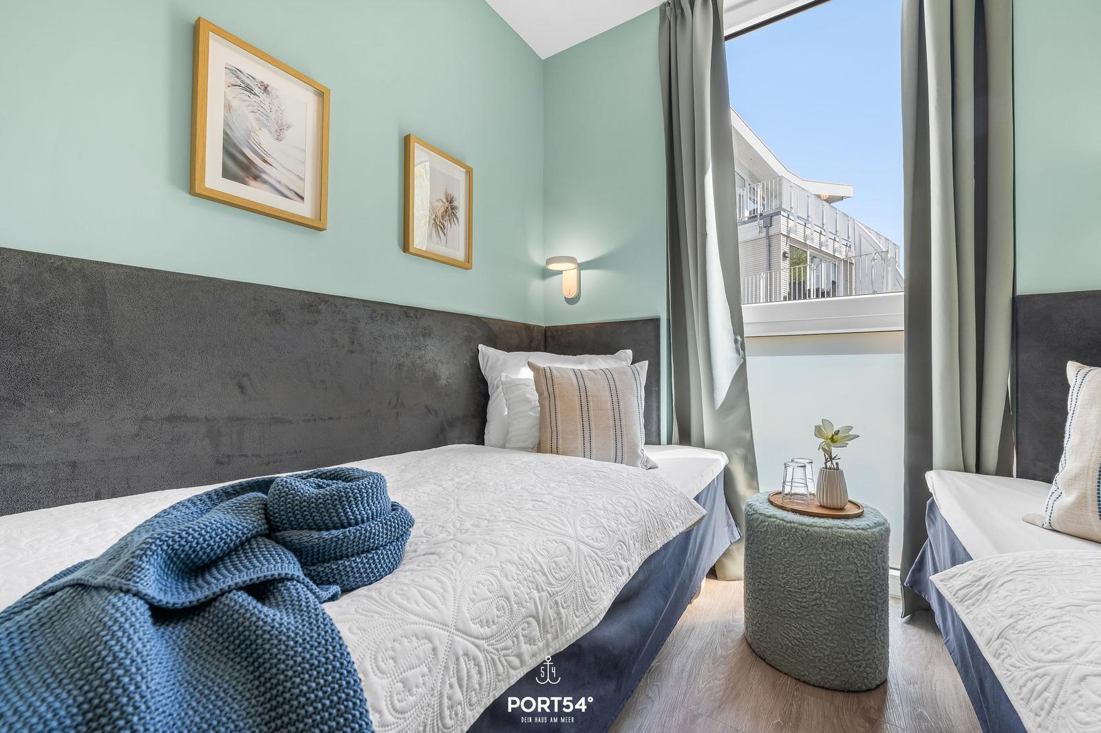 Zimmer mit zwei Betten, hellblauen Wänden und Blick auf Balkon.