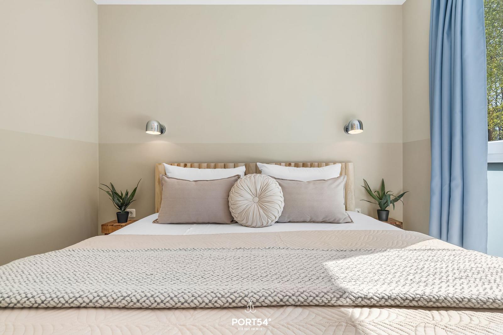 Schlafzimmer mit Bett, Kopfteil und zwei Nachttischen mit Pflanzen.